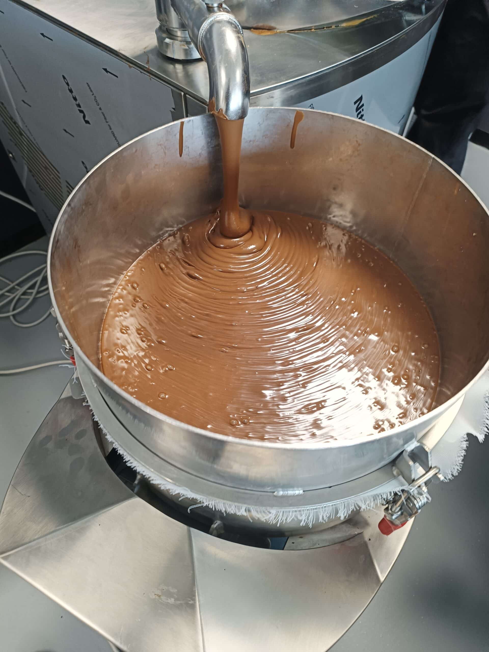 Chocolat fondu coulant d'un robinet en inox dans une grande cuve Nitto, créant des ondulations brillantes et onctueuses.