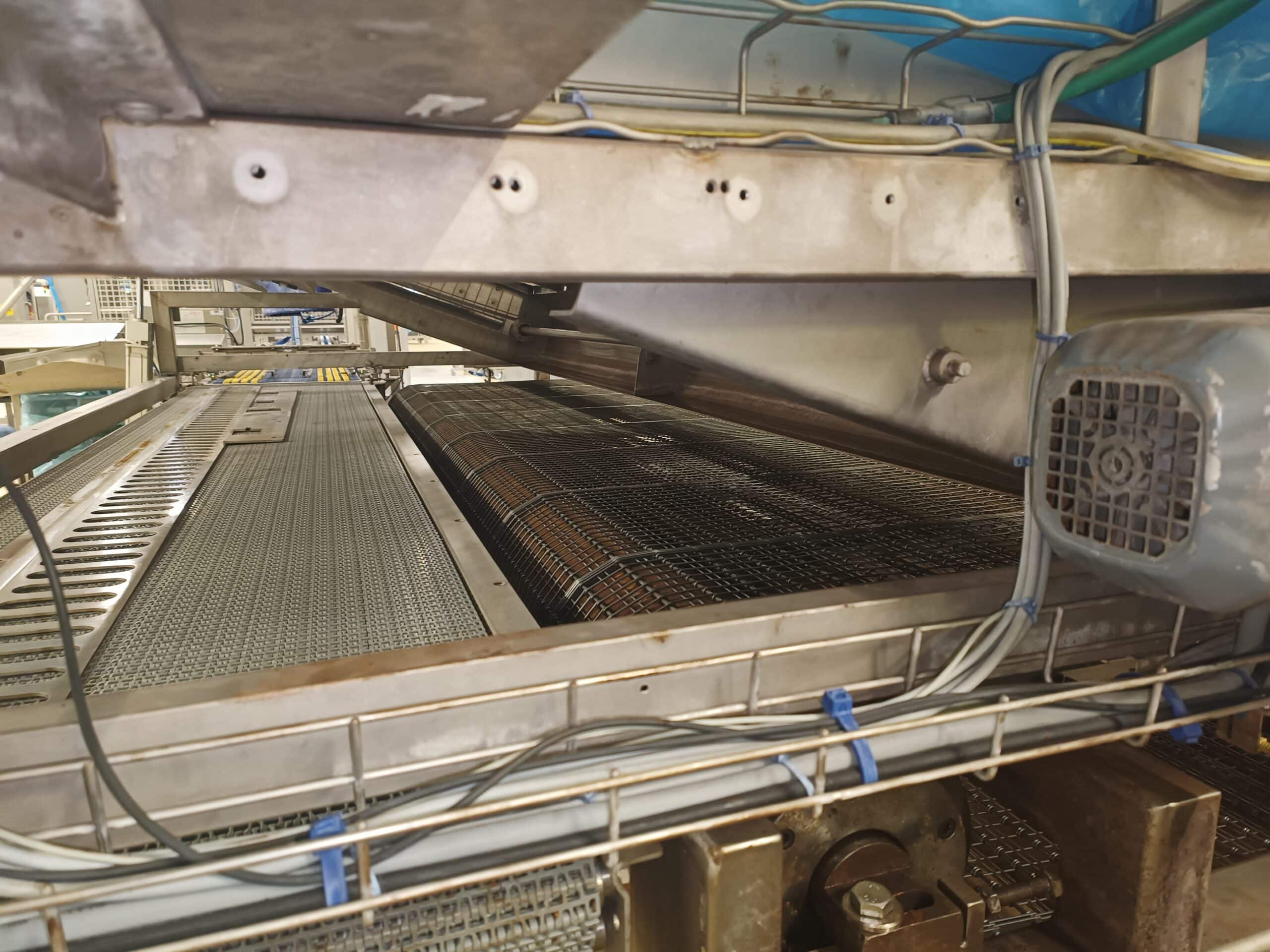 Convoyeur à bande métallique en inox avec moteur électrique et câblage sécurisé par des attaches bleues.