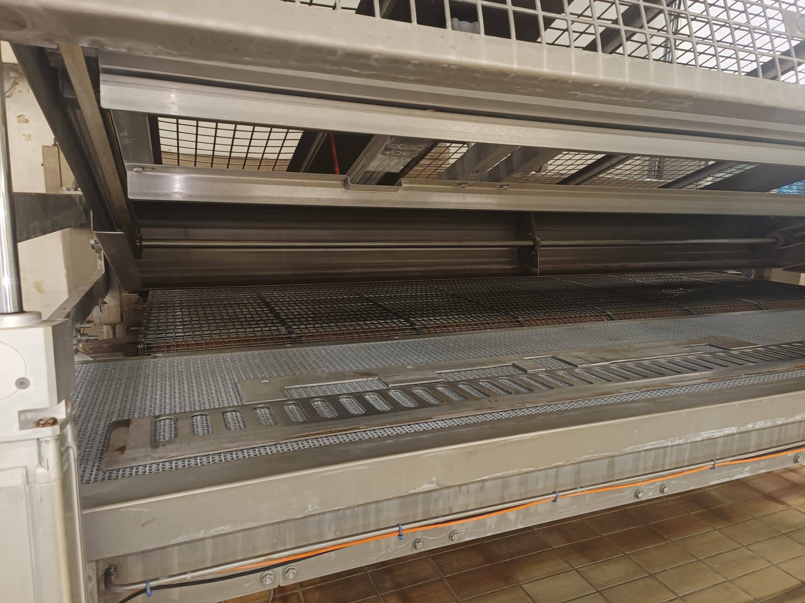 Convoyeur industriel métallique à grille et fentes pour le tri en usine agroalimentaire.