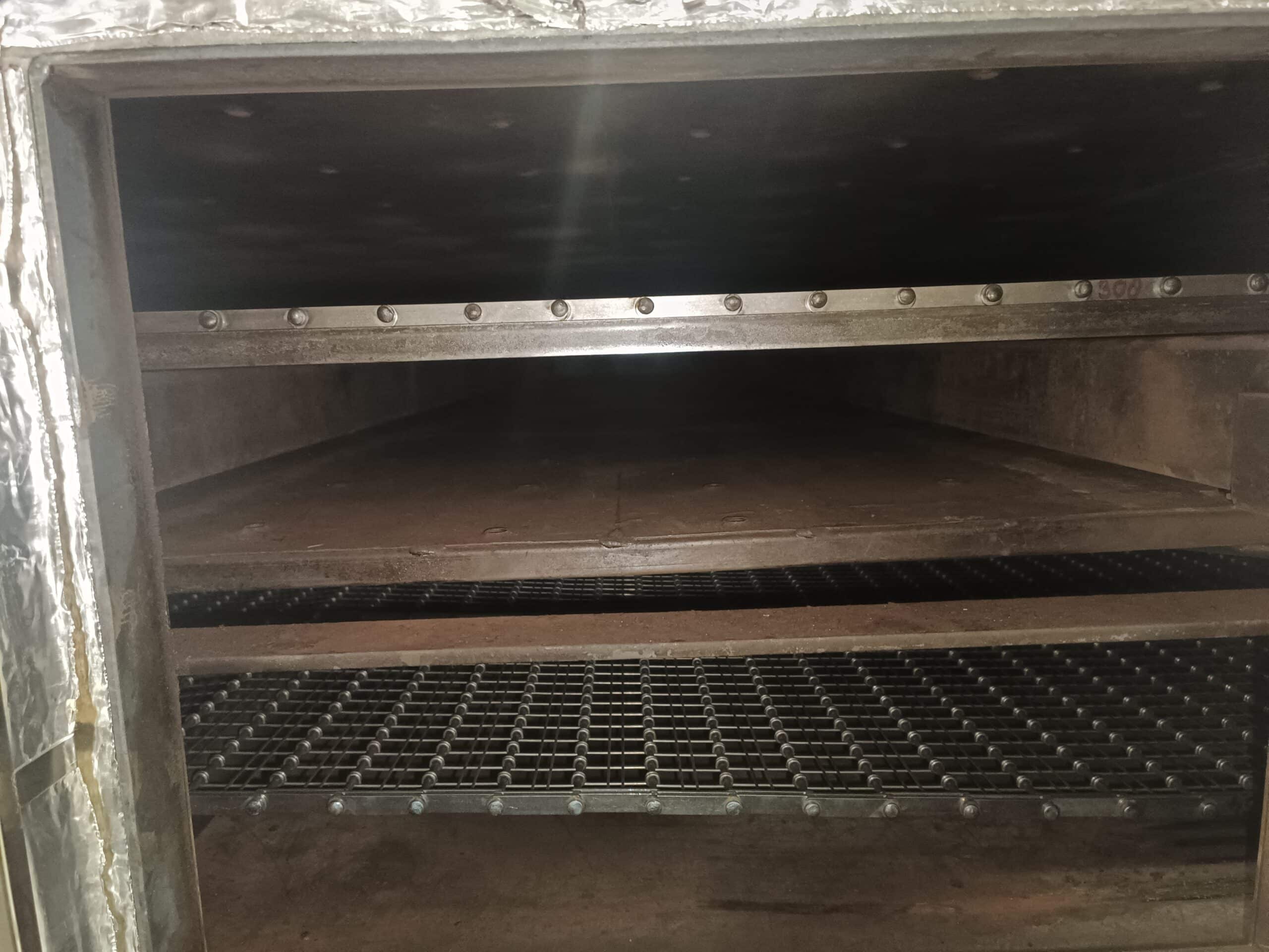 Intérieur de four industriel avec étagères métalliques, grille à mailles et parois isolées thermiquement.