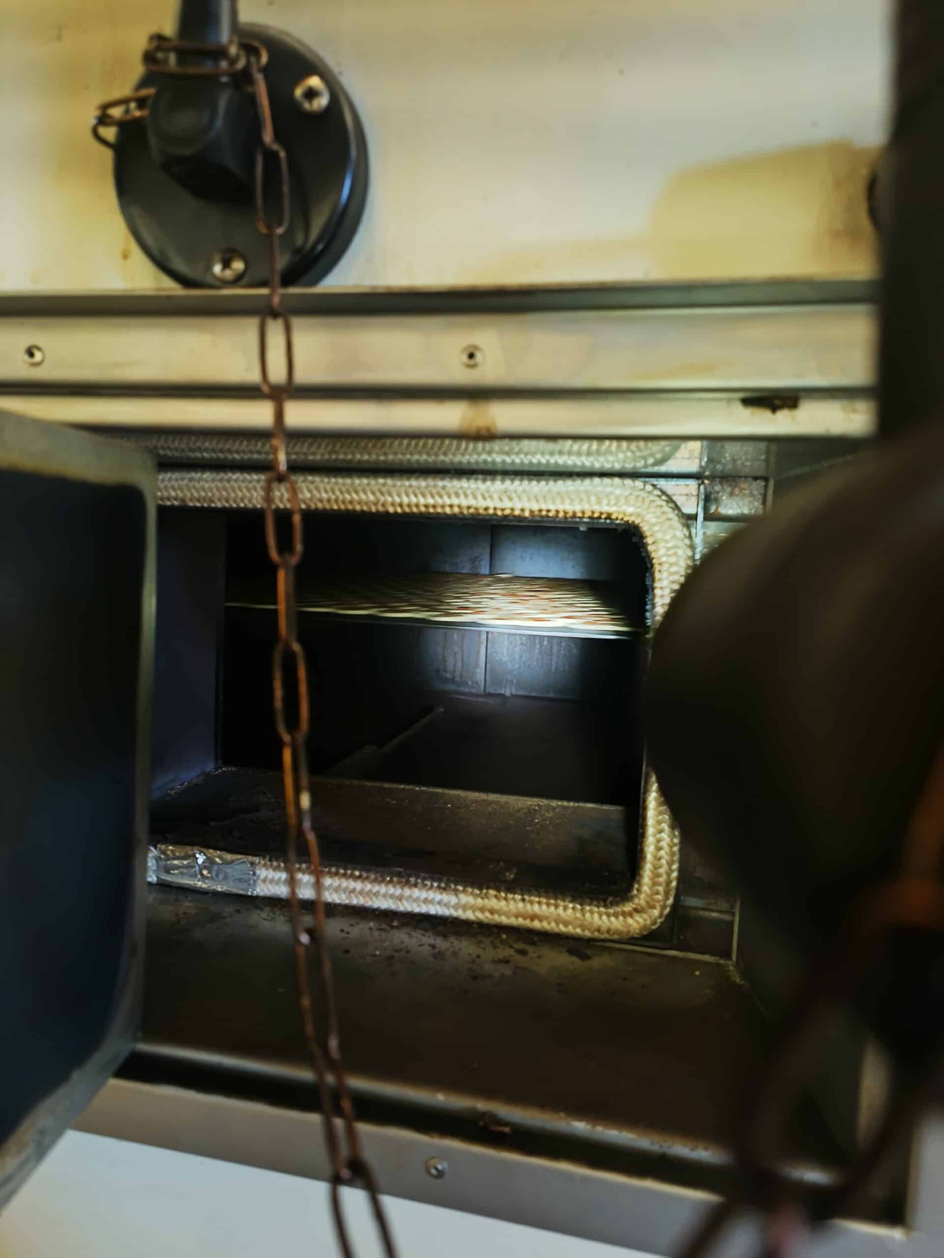 Intérieur d'un four industriel avec joint en corde haute température, étagère métallique et chaîne devant l'ouverture.