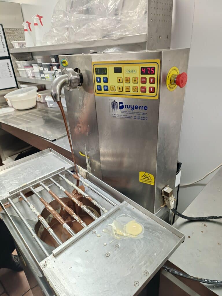 Tempéreuse à chocolat Bruyerre versant du chocolat fondu sur une grille dans un atelier de pâtisserie.