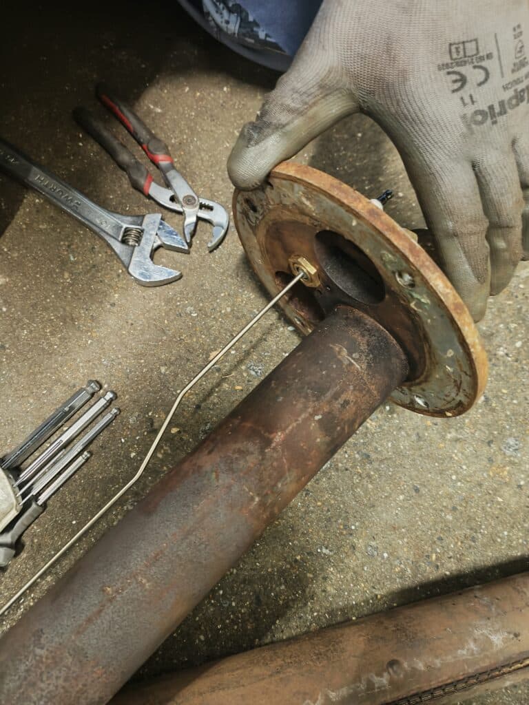 Main gantée inspectant une bride métallique rouillée avec clé Wurth, pince et clés Allen sur béton.